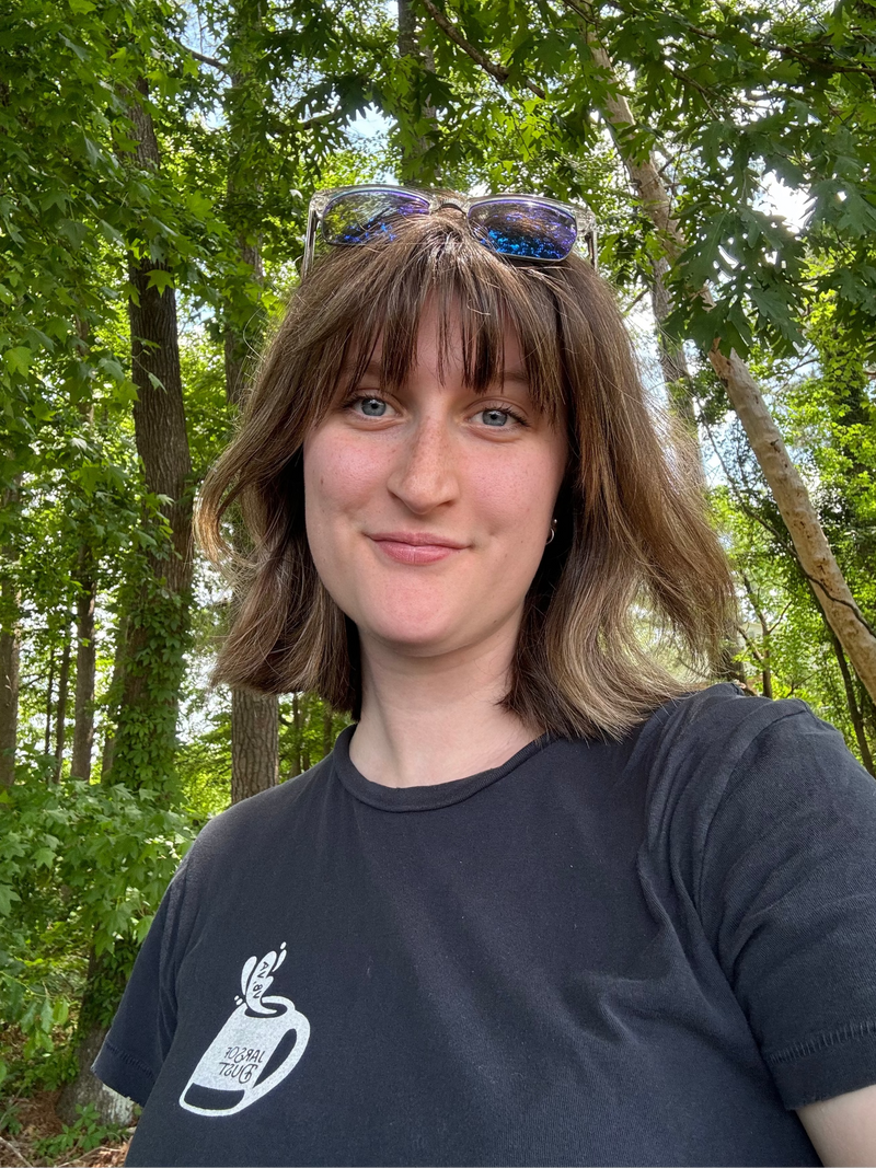 Carly Melvin standing in a forest wearing a black t-shirt with a logo.